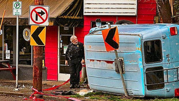 A Central Precinct officer examined the smashed and wedged-in van, while waiting for a second and larger tow truck to arrive to remove it from the sidewalk on Milwaukie Avenue near S.E. Nehalem Street in Sellwood.
